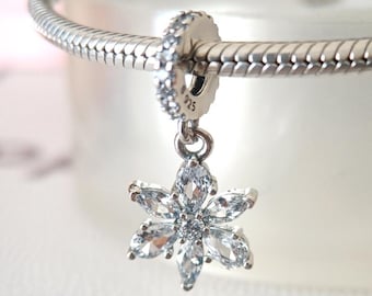 May include: A silver charm with a flower design. The charm features a flower pendant with clear, sparkling crystals. The charm is attached to a silver bracelet. The charm is a jewelry accessory.