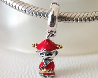 May include: A silver charm with a red and gold figure, possibly a traditional character. The figure is wearing a red hat and robe, holding a gold object. The charm is suspended from a silver bracelet.