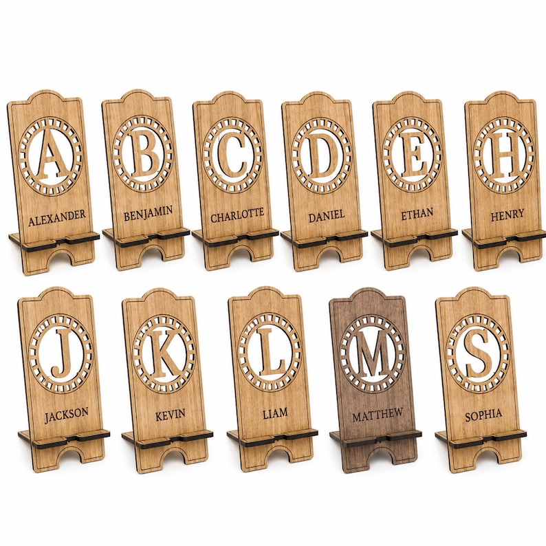 Puede incluir: Una colecci&oacute;n de once soportes de madera para tel&eacute;fonos, cada uno con un recorte circular con una letra may&uacute;scula cortada a l&aacute;ser y un nombre grabado debajo. Los soportes tienen una base con muescas y un acabado de madera clara.