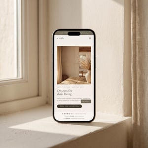 May include: A smartphone displaying a website titled Ställe with the text Objects for slow living, featuring a photograph of a ceramic vase with dried grass on a wooden table, along with a Shop the Collection button and a 4.9 star rating.