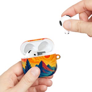 以下が含まれることがあります： 白のワイヤレスイヤホンと、それに合うケース。ケースは開いており、中にイヤホンが1つ入っています。ケースは、山、木、夕日を特徴とするカラフルな風景デザインで塗装されています。