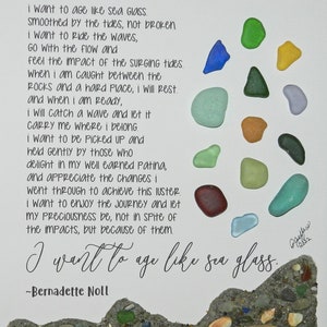 May include: A mixed media artwork featuring a poem about aging like sea glass. The artwork includes colorful sea glass pieces, sand, pebbles, and driftwood. The text reads "I want to age like sea glass" by Bernadette Noll.
