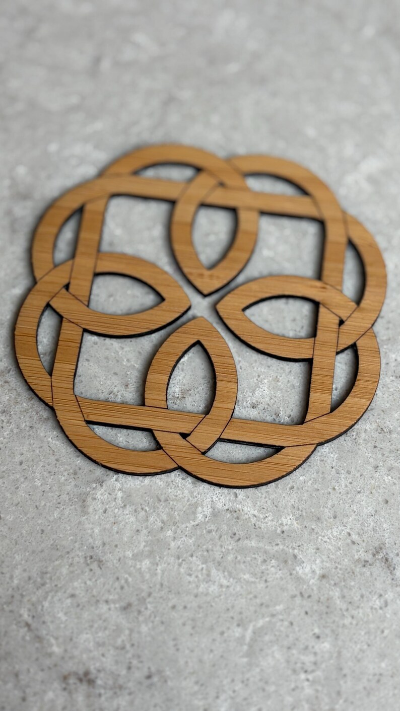 May include: A wooden coaster with a Celtic knot design. The coaster is made of light brown wood with a dark brown outline. The interlocking design is circular and symmetrical, suitable for home decor.