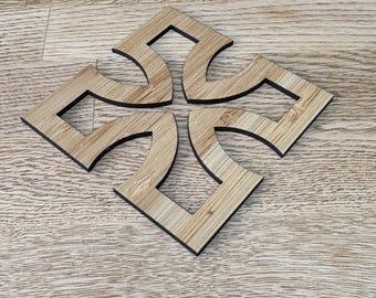 May include: Four wooden, interlocking pieces arranged to form a stylized cross shape. The pieces have a light brown wood grain finish with dark edges, set against a light wood grain surface.