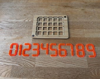 May include: A wooden grid-like board with a series of rectangular cutouts, and a set of orange, digital-style numbers from 0 to 9. The items are arranged on a wooden surface.