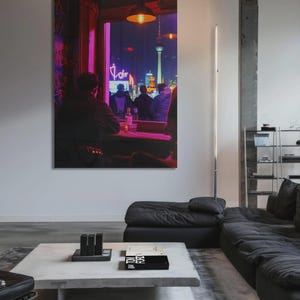Op de afbeelding: Een groot ingelijst kunstwerk toont een nachtelijk stadsgezicht gezien door een raam. De scène omvat figuren aan een tafel, neonreclame en een verlichte toren. Het kunstwerk hangt aan een witte muur in een moderne woonkamer.