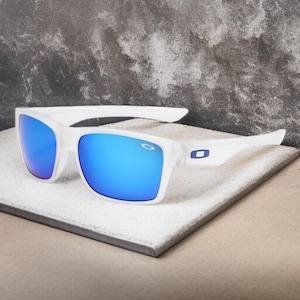 May include: White sunglasses with blue mirrored lenses. The sunglasses have a rectangular frame and a small blue logo on the temple. The lenses reflect a bright blue color.