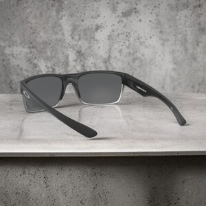 May include: Black sunglasses with gray lenses. The sunglasses have a rectangular frame with a clear lower rim. The arms are black and curve slightly. The text "TWINFACE" is visible on the right arm.