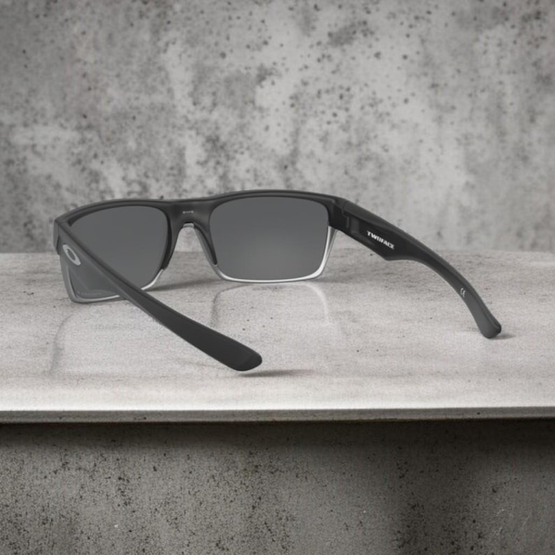May include: Black sunglasses with gray lenses. The sunglasses have a rectangular frame with a clear lower rim. The arms are black and curve slightly. The text "TWINFACE" is visible on the right arm.