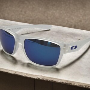 May include: White-framed sunglasses with blue reflective lenses. The sunglasses have a rectangular shape and a small blue logo on the temple. The lenses are a vibrant blue color, and the frame is a translucent white.