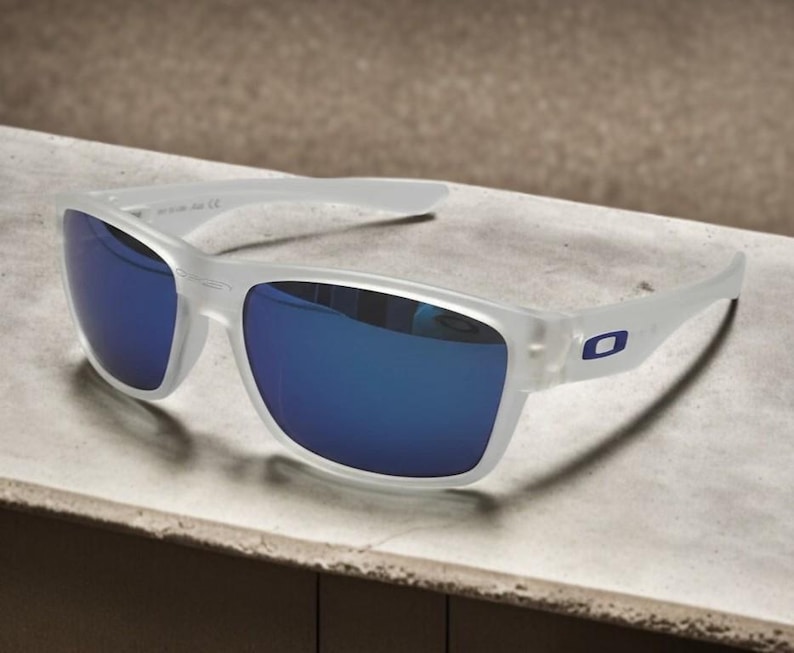 May include: White-framed sunglasses with blue reflective lenses. The sunglasses have a rectangular shape and a small blue logo on the temple. The lenses are a vibrant blue color, and the frame is a translucent white.