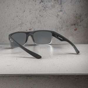 May include: Black sunglasses with gray lenses. The sunglasses have a rectangular frame and the text "TWINFACE" is visible on the temple. The sunglasses are resting on a light gray surface.