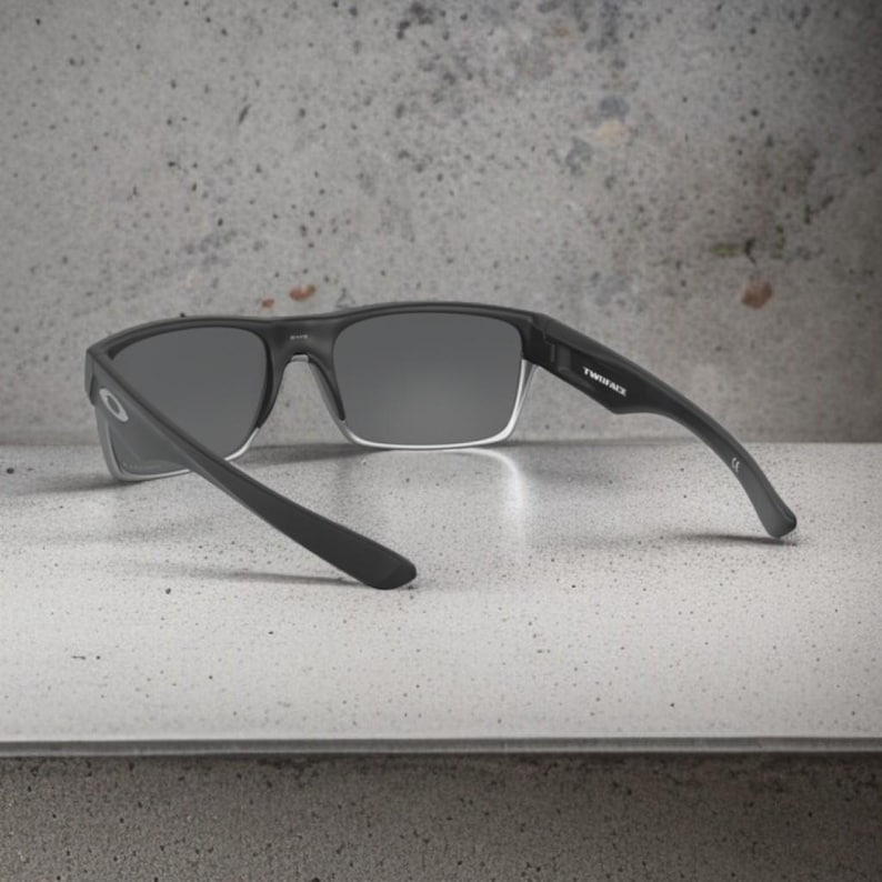 May include: Black sunglasses with gray lenses. The sunglasses have a rectangular frame and the text "TWINFACE" is visible on the temple. The sunglasses are resting on a light gray surface.