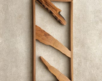 Può includere: Opera d'arte da parete in legno rettangolare. Presenta tre forme irregolari in legno all'interno della cornice, creando un design astratto. Il legno ha una tonalità calda e naturale, per un tocco rustico.