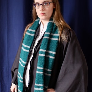 May include: A woman wearing a black robe with a green and white striped scarf. She is wearing glasses and has long brown hair.