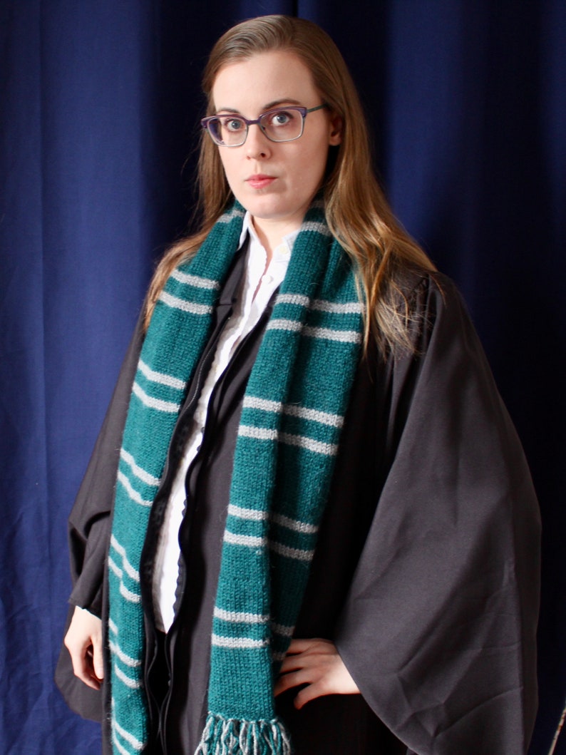 May include: A woman wearing a black robe with a green and white striped scarf. She is wearing glasses and has long brown hair.