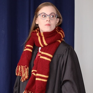 May include: A person wearing a black robe with a red and gold striped scarf. The scarf has tassels on the ends.