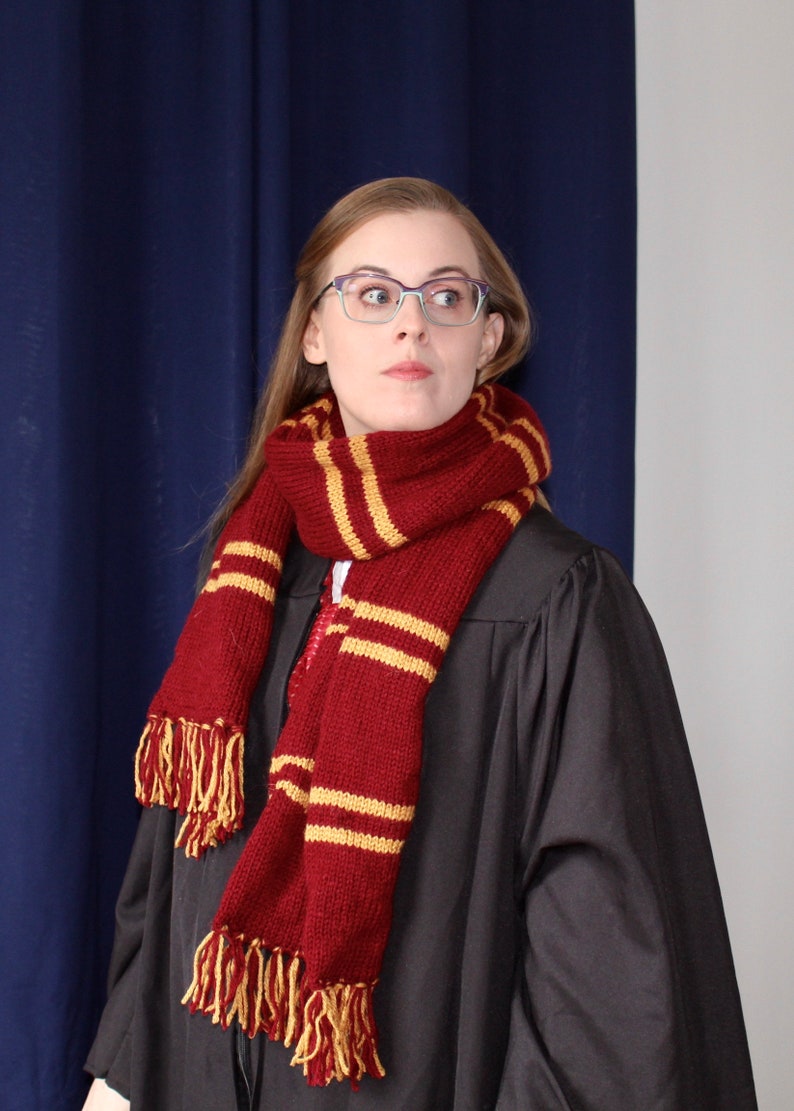 May include: A person wearing a black robe with a red and gold striped scarf. The scarf has tassels on the ends.
