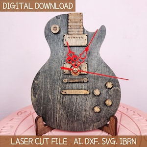 May include: A wooden guitar-shaped clock with red clock hands and a gold center. The clock has a gray finish with wooden accents and is displayed on a wooden stand. The words "DIGITAL DOWNLOAD" and "LASER CUT FILE AI. DXF. SVG. IBRN" are visible.