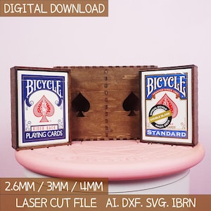 May include: A wooden playing card holder with two Bicycle card decks. The decks are in wooden frames, and the holder has spade cutouts. The text "DIGITAL DOWNLOAD" is at the top. The bottom text says "2.6MM / 3MM / 4MM LASER CUT FILE AI. DXF. SVG. IBRN."