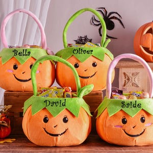 May include: Orange pumpkin-shaped Halloween treat bags with green leaf trim and smiling faces. Each bag has a name on it: Bella, Oliver, David, and Saide. A carved pumpkin and other Halloween decorations are in the background.
