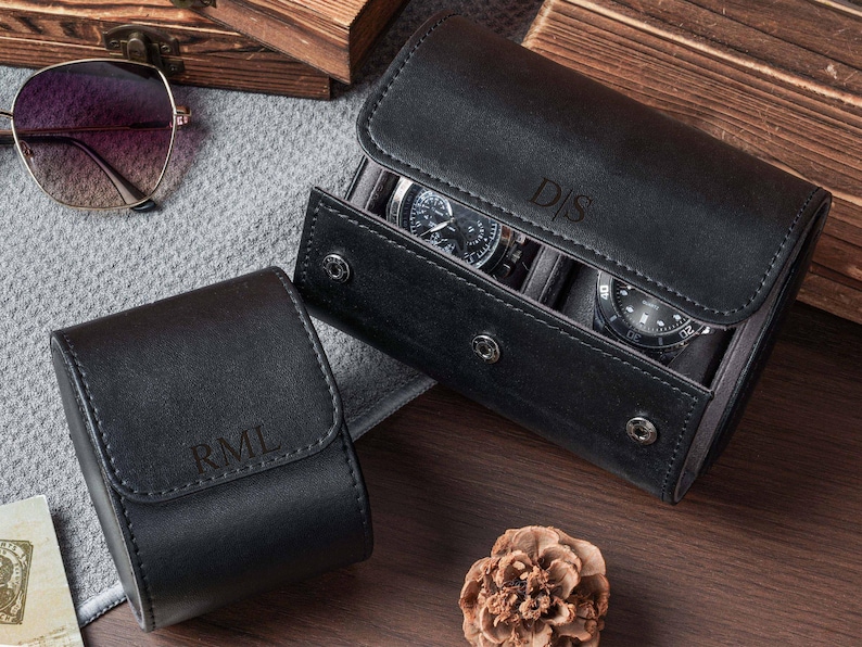 May include: Two black leather watch cases with snap closures. One smaller case features the embossed initials RML, while the larger case holds two wristwatches and is embossed with the initials D|S on the front flap.