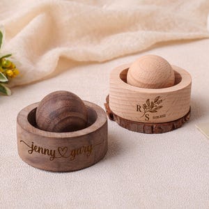 May include: Two wooden ring boxes, one dark brown and one light brown, each with a spherical top. The dark brown box is engraved with "jenny ♡ gary". The light brown box has a floral design and the date "11.09.2022".