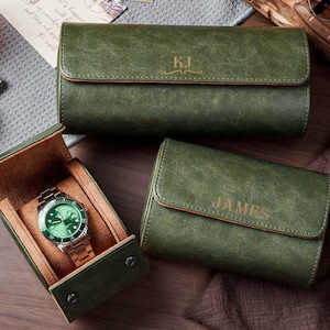 May include: Three dark green watch cases with a smooth finish and tan interior lining. One case is open, displaying a silver watch with a green face. The other two cases are closed, with the names KJ and JAMES engraved on the front flaps.