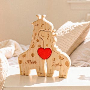 May include: Wooden giraffe puzzle with a red heart in the center. The puzzle is engraved with the words "Mom" and "Sophia". The giraffe puzzle is made of light-colored wood and has a whimsical design.