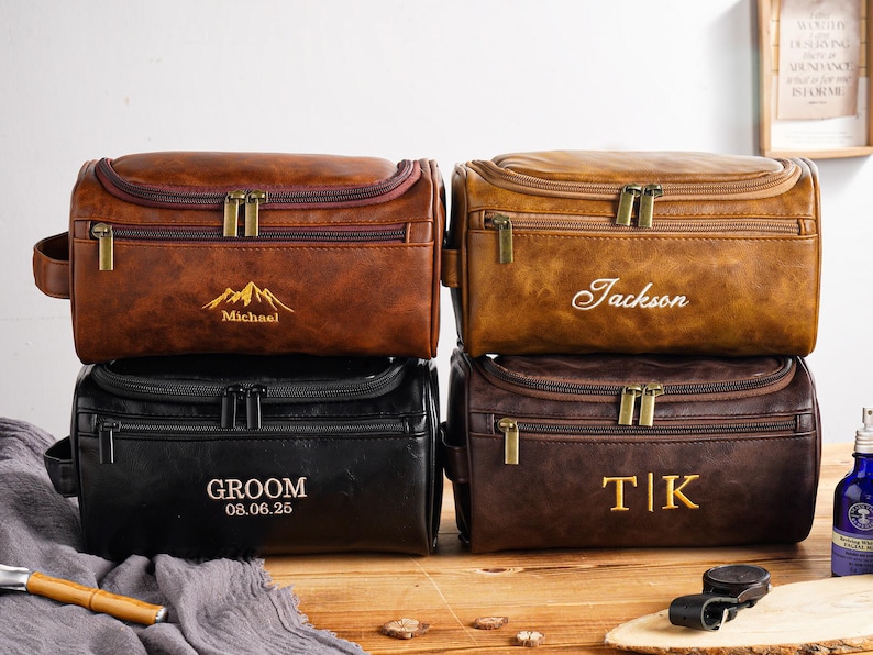 May include: Four personalised leather wash bags in shades of brown and black. Each bag has a zip closure and a handle. The bags are embossed with names, initials, and a mountain graphic. The text "GROOM 08.06.25" is also visible.