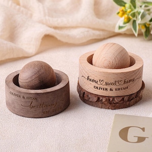 May include: Two wooden ring boxes with a round top and a wooden sphere inside. One box is engraved with "Oliver & Ehtan" and "Brittany EST. 2024". The other box is engraved with "home sweet home" and "Oliver & Ehtan".