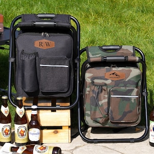 May include: Two portable folding chair backpacks, one solid black and one camouflage print. Each features a black metal frame, a zippered main compartment, a front pocket with a reflective strip, a side drink holder, and a leather-like patch.