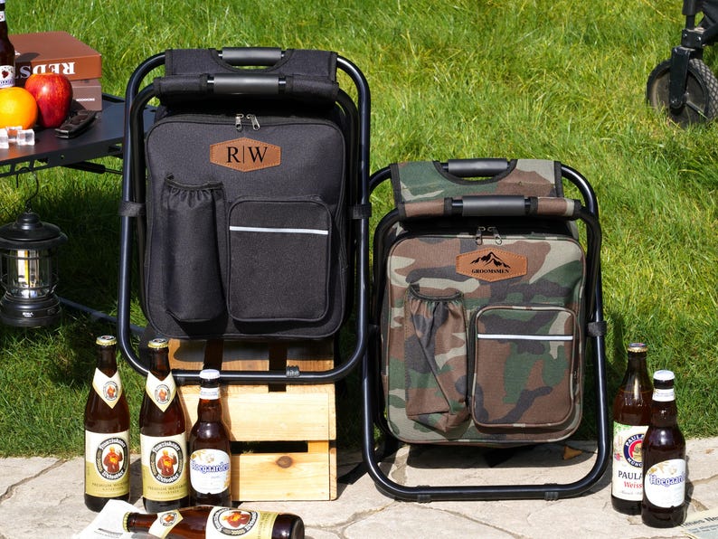 May include: Two portable folding chair backpacks, one solid black and one camouflage print. Each features a black metal frame, a zippered main compartment, a front pocket with a reflective strip, a side drink holder, and a leather-like patch.