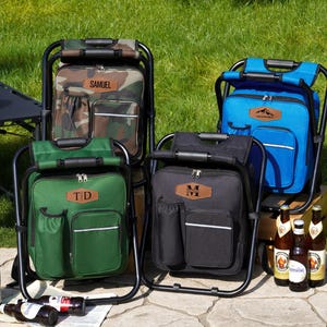 May include: Four portable folding chair backpacks in camouflage, blue, green, and black. Each features a black metal frame, a main zippered compartment, a front pocket, a side drink holder, and a leather-like patch with personalized text.