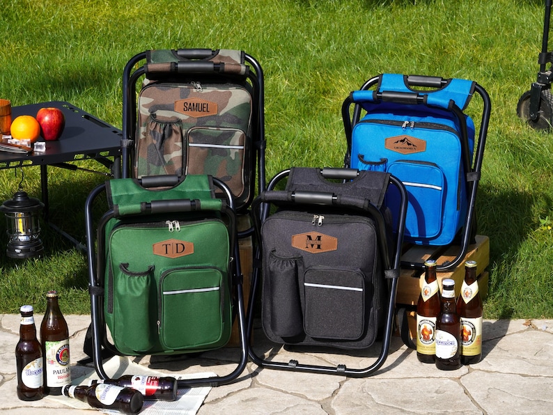 May include: Four portable folding chair backpacks in camouflage, blue, green, and black. Each features a black metal frame, a main zippered compartment, a front pocket, a side drink holder, and a leather-like patch with personalized text.