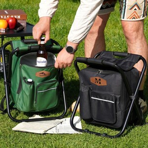 May include: Two portable cooler backpacks with integrated folding stools, one in forest green and one in black. Each bag features a front zippered pocket, a side bottle holder, and a brown leather-like patch with custom text branding.