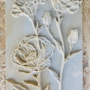 May include: A rectangular, light beige stone carving with a floral design. The relief shows several flowers, buds, and leaves with detailed textures. The artwork is likely for decorative purposes.