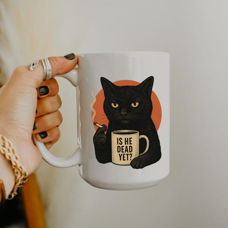 May include: White ceramic mug with a black cat illustration, yellow eyes, holding a cigarette and a mug that says "IS HE DEAD YET?". The cat is set against an orange circle.