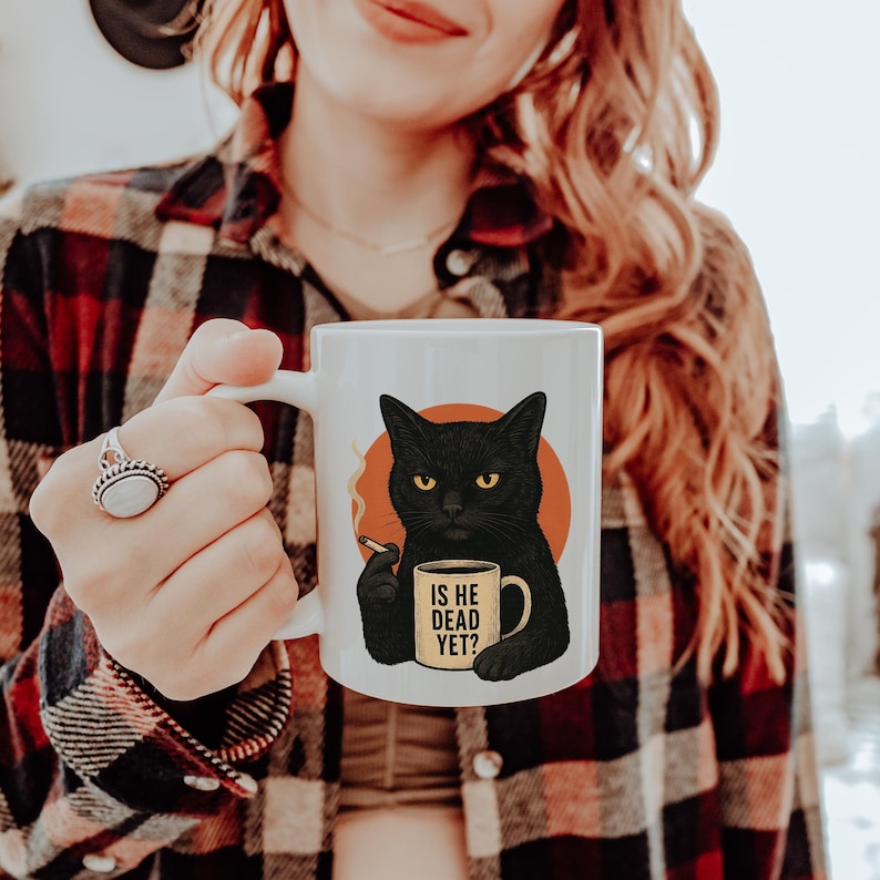 May include: White ceramic mug with a black cat illustration. The cat holds a cigarette and a mug with the text "IS HE DEAD YET?". The cat is set against an orange circle. The mug is a standard size.