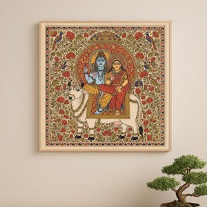 May include: A framed, colorful painting depicting two figures riding a white bull. The figures are adorned in traditional Indian clothing, set against a backdrop of floral patterns and birds. The artwork is framed in a light wood.