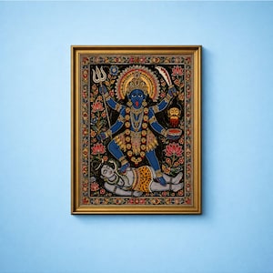 May include: A framed painting depicting a blue-skinned deity with multiple arms, holding a trident and a sword, standing over a reclining figure. The artwork features a floral border, a golden halo, and a necklace of skulls, all set in a gold frame.