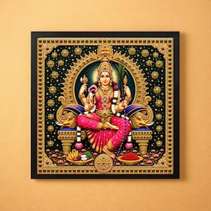 May include: A square framed wall art print depicting a deity seated on an ornate golden throne with elephant motifs. The figure wears a pink sari and gold jewelry, holding a lotus and a sugarcane stalk, surrounded by offerings of fruit and red powder.