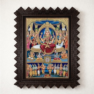 May include: A framed print featuring a central seated deity in a red and gold garment, surrounded by multiple smaller figures in colorful traditional attire. The artwork is set against a deep blue background and enclosed in a dark brown ornate frame.