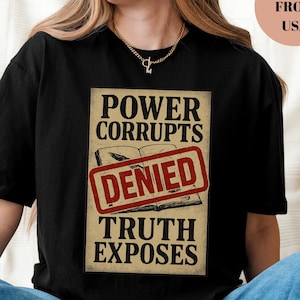 May include: Black t-shirt with a graphic design featuring the text "POWER CORRUPTS DENIED TRUTH EXPOSES" over an image of an open book. The word "BLACK" is printed at the bottom of the shirt.