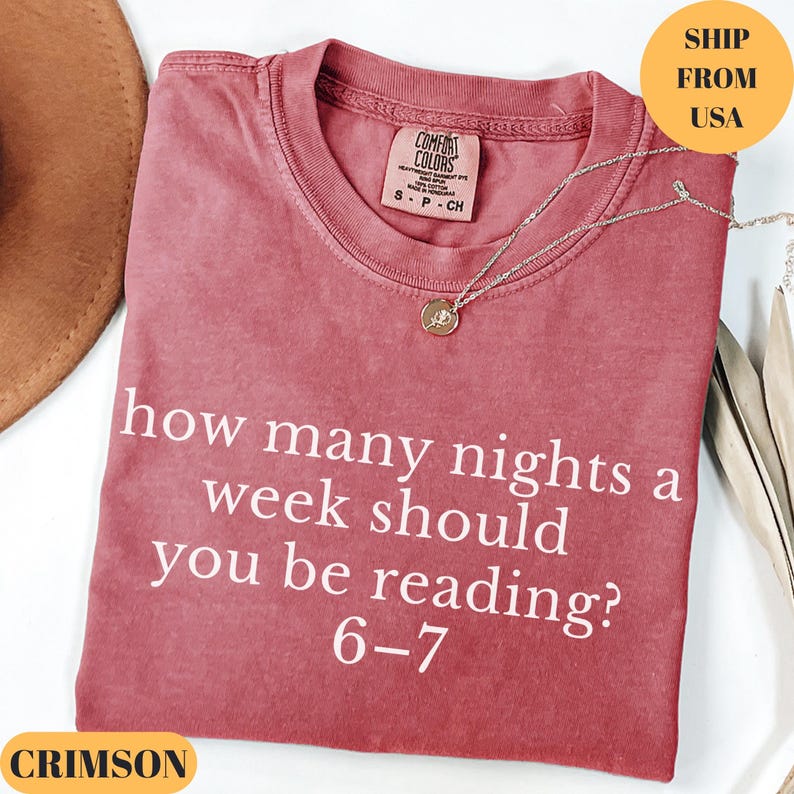 Puede incluir: Camiseta de color carmes&iacute; con el texto blanco "how many nights a week should you be reading? 6-7". La camiseta tiene cuello redondo y una peque&ntilde;a etiqueta. Una cadena de plata con un colgante est&aacute; sobre la camiseta.