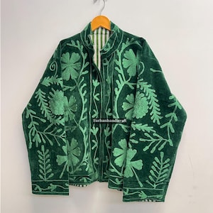 May include: A dark green velvet jacket with intricate light green floral embroidery. The jacket has a high collar and a full-length zipper. The lining is a striped pattern. The text "Farhanhandicraft" is visible.