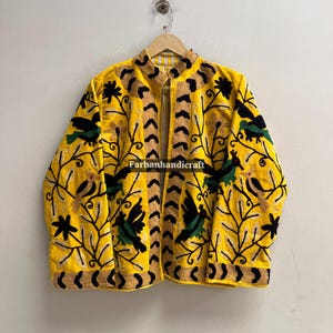 May include: A yellow jacket with intricate embroidery featuring black birds and floral patterns. The jacket has a high collar and a zipper closure. The text "Farhanhandicraft" is visible on the jacket.