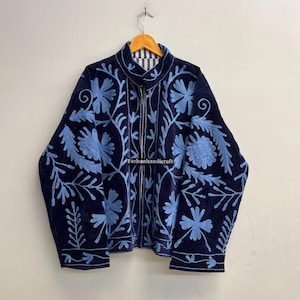 Peut inclure: Veste bleu marine avec broderies florales bleu clair. La veste est entièrement zippée et possède un col montant. L'intérieur est doublé d'un motif à rayures. Le texte "Farhanhandicraft" est visible.