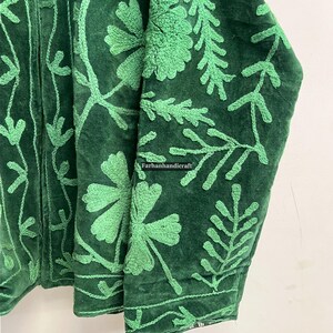 May include: Close-up of a dark green jacket with intricate light green floral embroidery. The jacket's fabric appears to be velvet, with detailed stitching of leaves and flowers. The text "Farhanhandicraft" is visible.