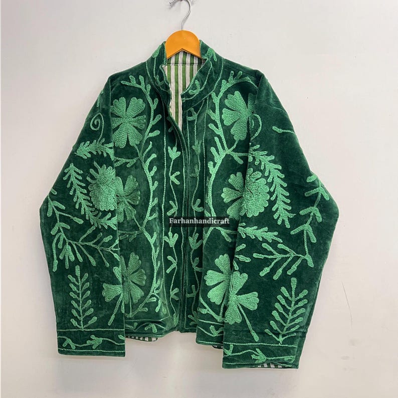 May include: A dark green velvet jacket with intricate light green floral embroidery. The jacket has a high collar and a full-length zipper. The lining is a striped pattern. The text "Farhanhandicraft" is visible.